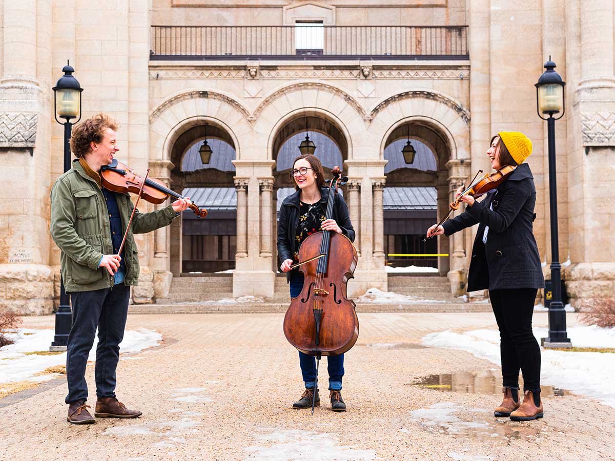 Close to Home artists John Sellick Alyssa Ramsay Jessie Ramsay standing outside playing instruments and laughing